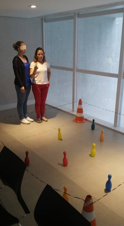 Imagem: Duas participantes, uma atuando como vidente e a outra com pessoa com deficiência visual, analisando a melhor forma para descrever o trajeto com obstáculos.